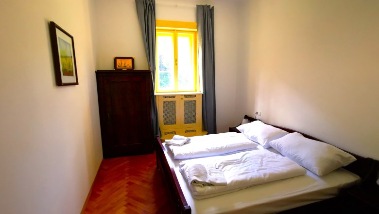 Schlafzimmer mit Doppelbett, Schrank und Fenster mit gelbem Rahmen.
