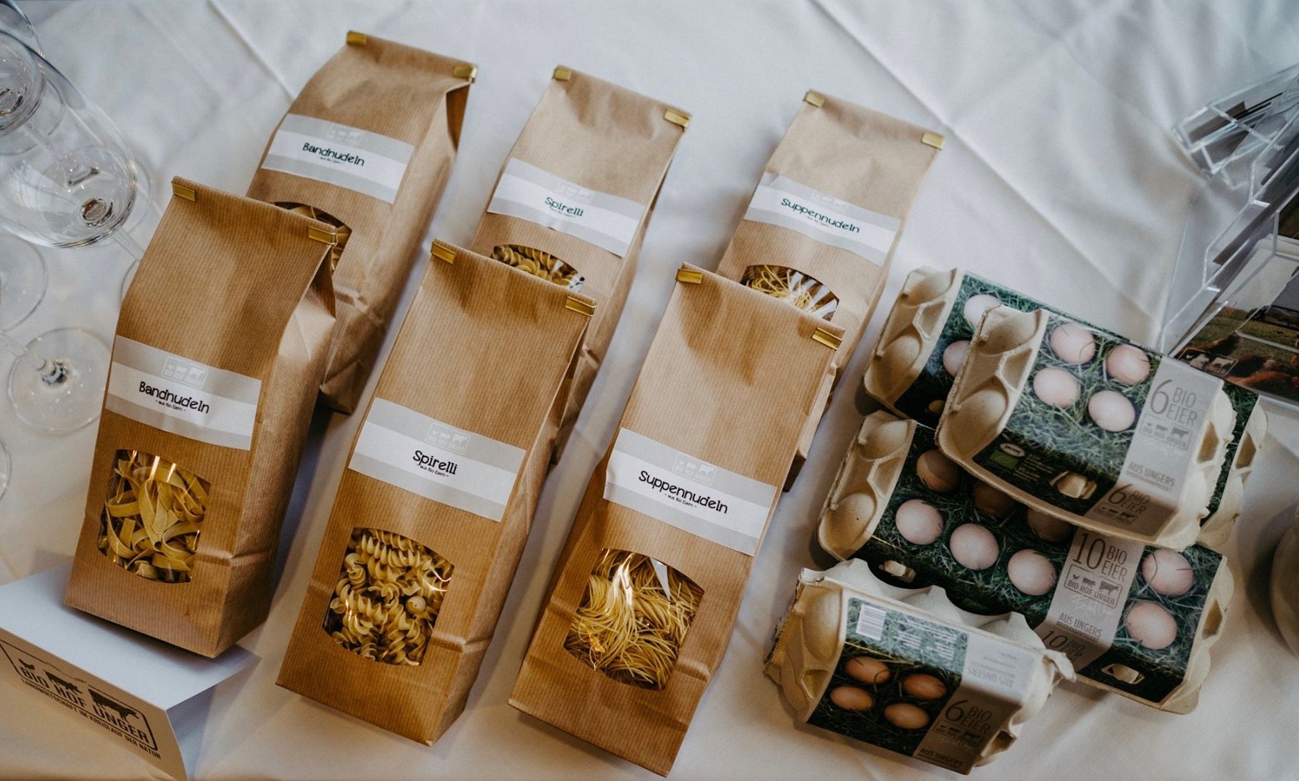 Produkte von Biohof Unger: Nudeln in braunen Tüten und Eierkartons auf einem Tisch.