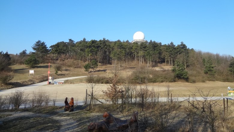 Landschaft mit H&uuml;gel, Wald und Radarkuppel unter blauem Himmel.