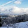 Winterlandschaft mit schneebedeckten B&auml;umen und H&uuml;geln unter blauem Himmel mit Wolken.
