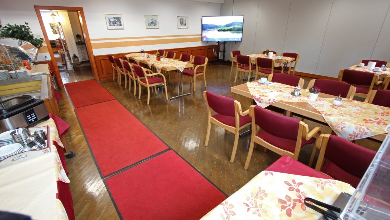 Ein Konferenzraum mit gedeckten Tischen, roten St&uuml;hlen und einem gro&szlig;en Bildschirm.