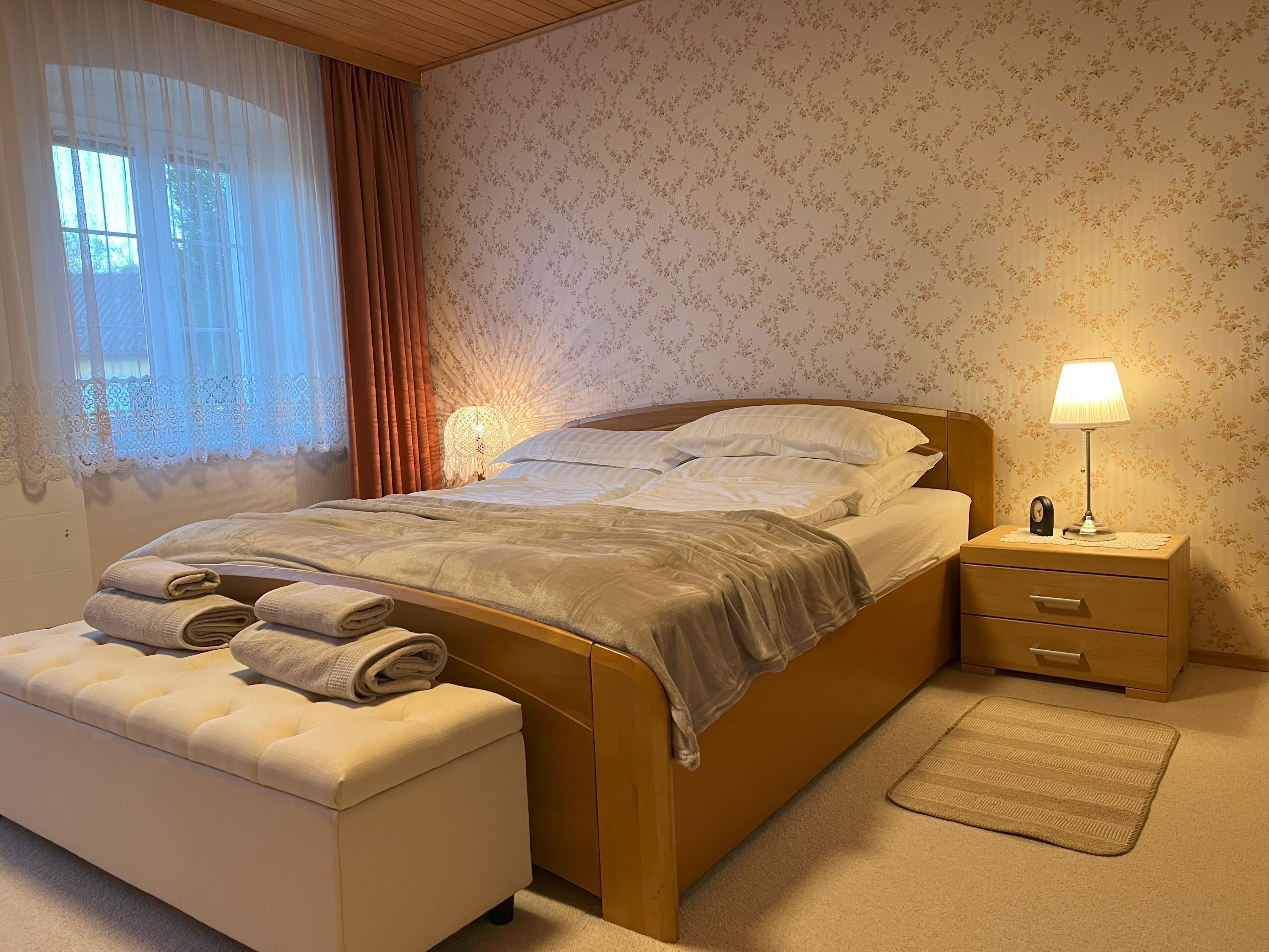 Gemütliches Schlafzimmer mit Doppelbett, Nachttischlampe und Fenster mit Vorhängen.