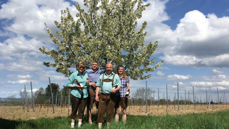 Vier Personen stehen vor einem blühenden Baum auf einem Feld.