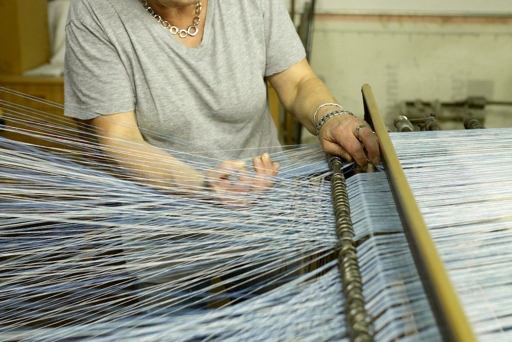 Person arbeitet an einem Webstuhl mit blauen Fäden.