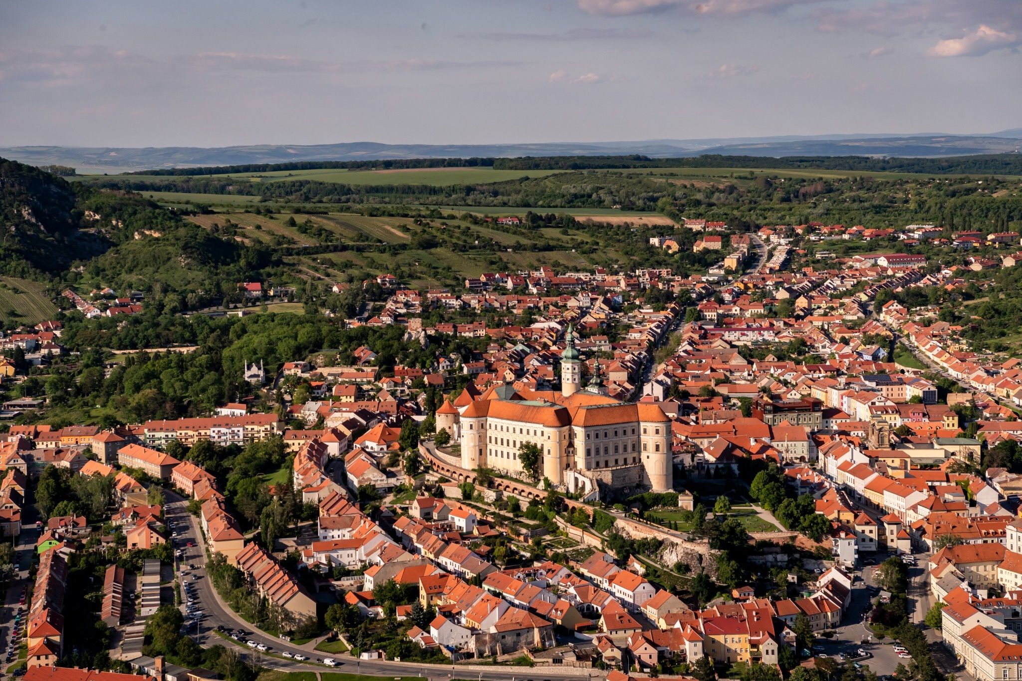 Luftaufnahme von Mikulov mit Schloss und Altstadt zwischen grünen Hügeln und Feldern.