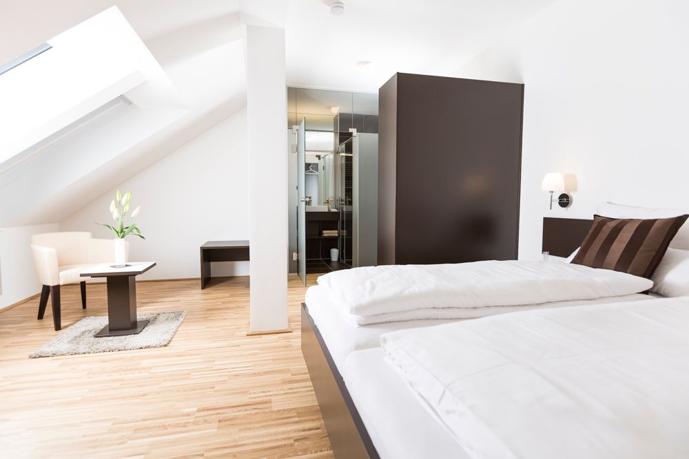 Modernes Gästezimmer mit Bett, Sessel und Tisch unter Dachschräge.