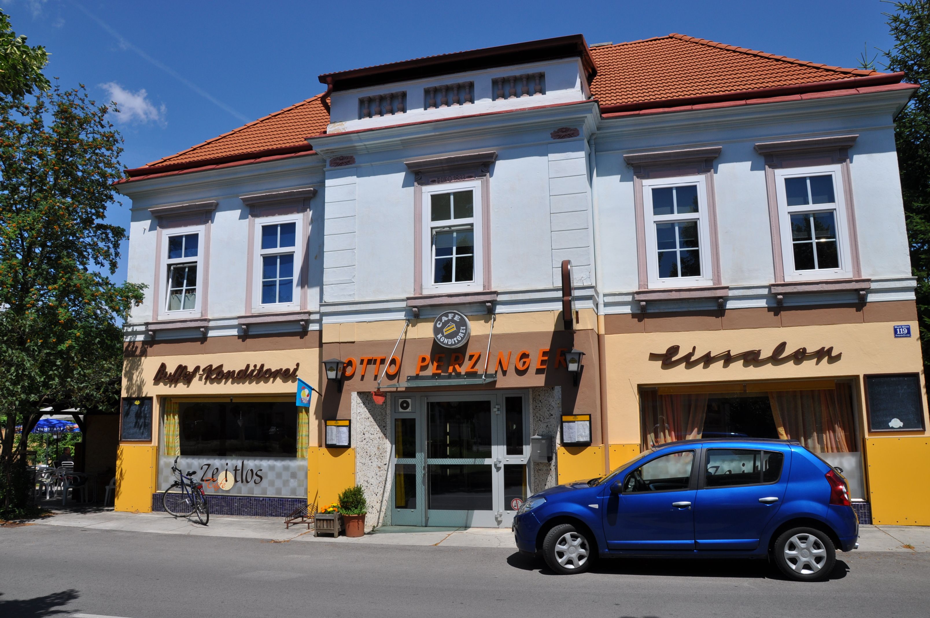 Außenansicht eines Cafés mit blauer Fassade und rotem Dach, davor ein blaues Auto geparkt.