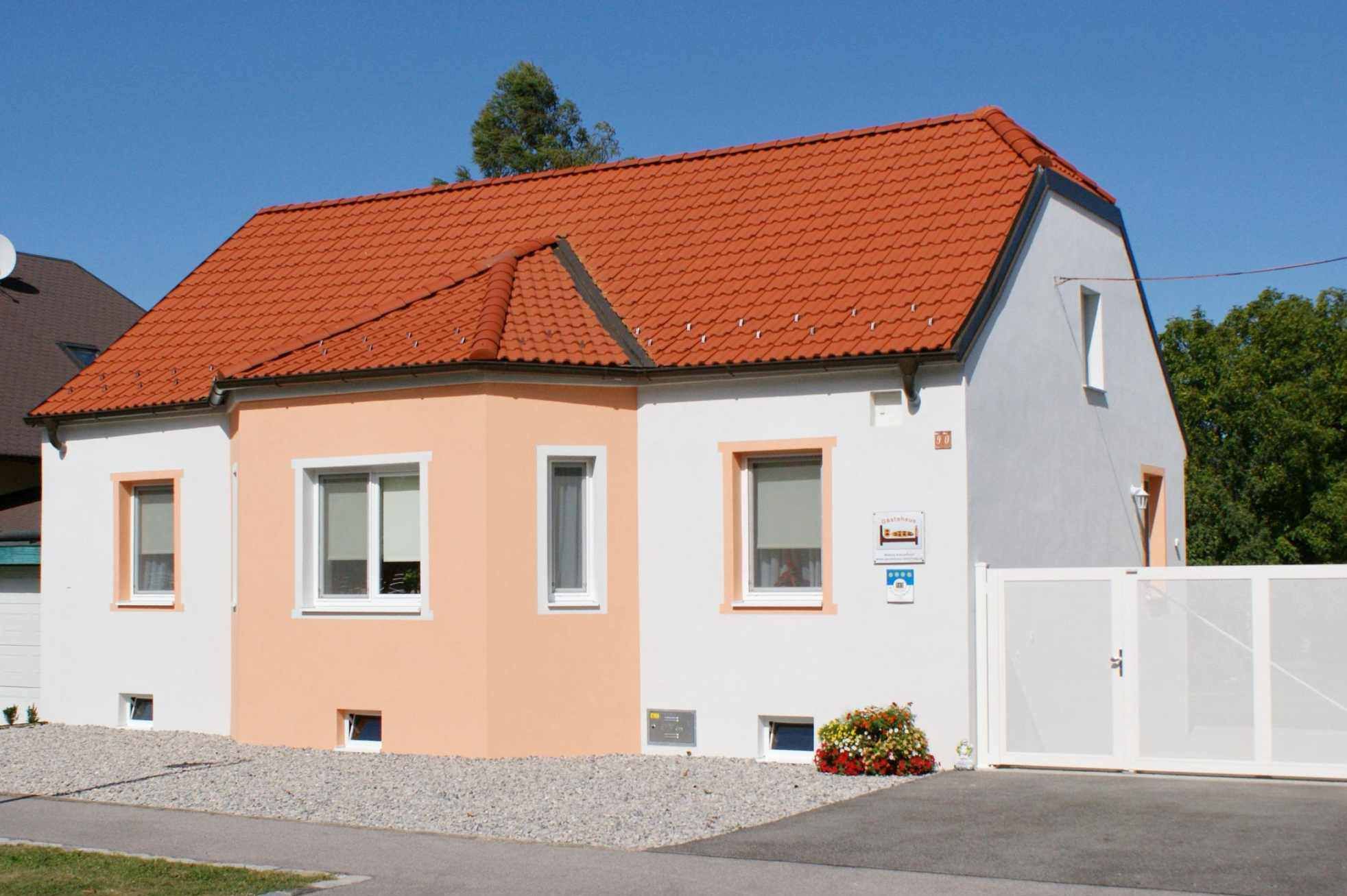 Ein kleines, einstöckiges Haus mit orangefarbenem Dach und weißer Fassade unter blauem Himmel.