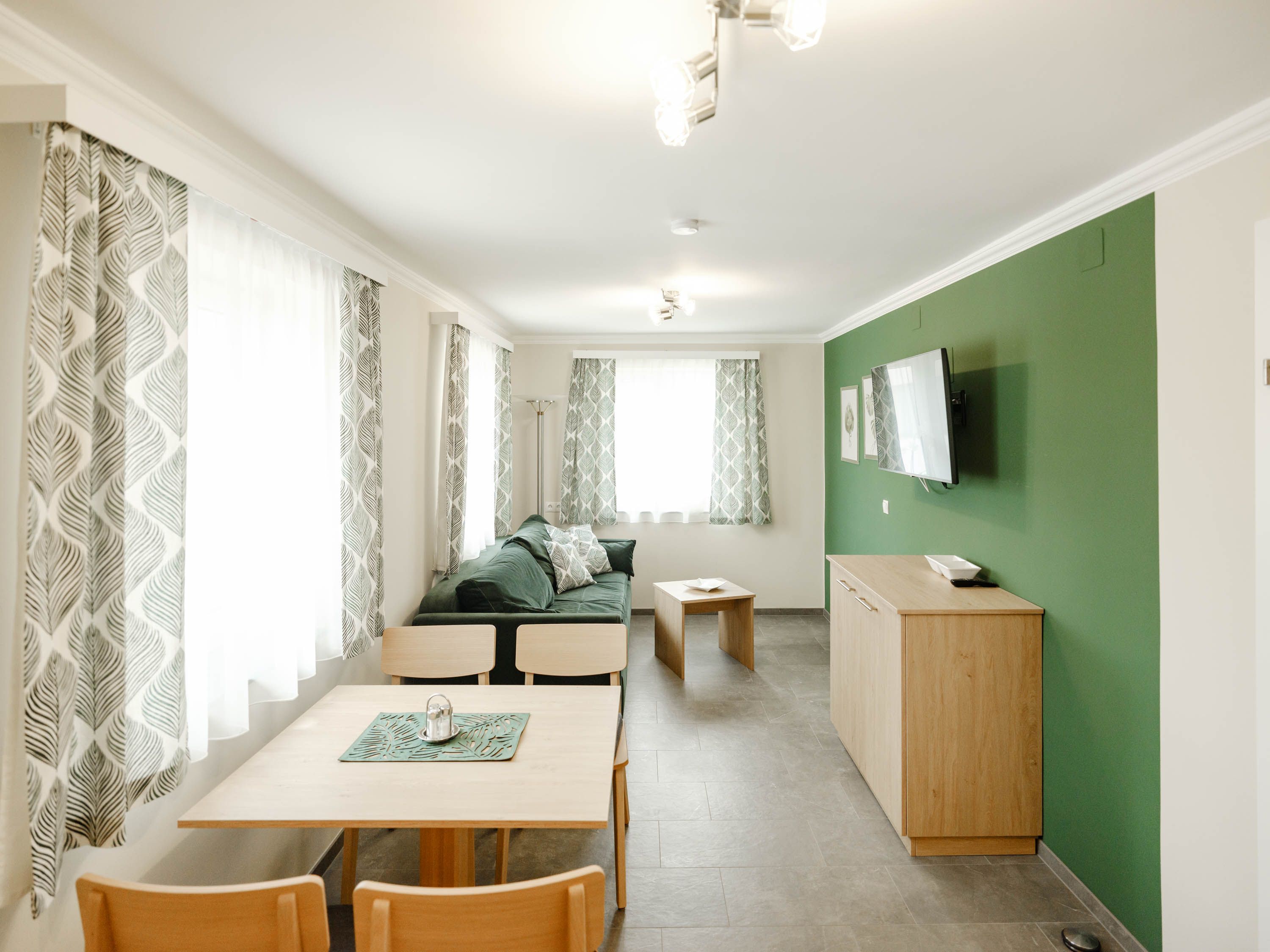 Modernes Wohnzimmer mit grüner Akzentwand, Holzmöbeln und gemusterten Vorhängen.