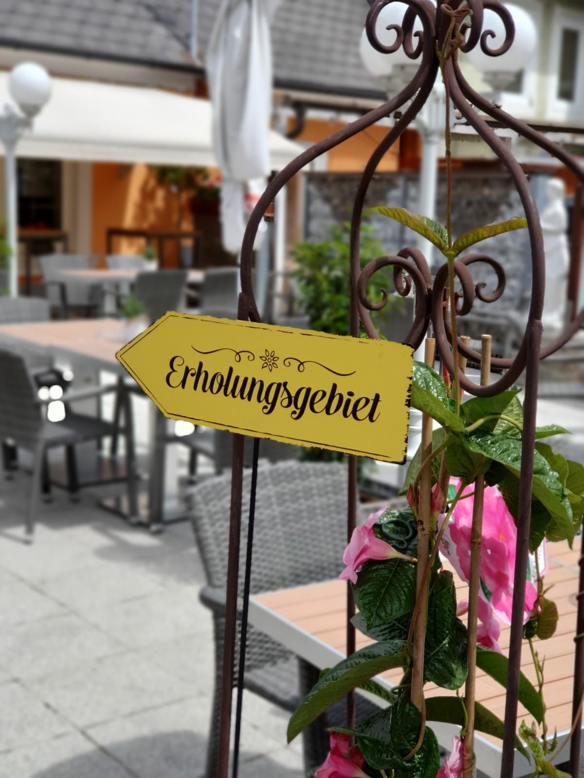 Ein Schild mit der Aufschrift 'Erholungsgebiet' in einem Café-Garten mit Tischen und Stühlen.