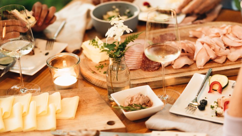 Ein gedeckter Tisch mit Brot, K&auml;se, Aufschnitt und Weingl&auml;sern.
