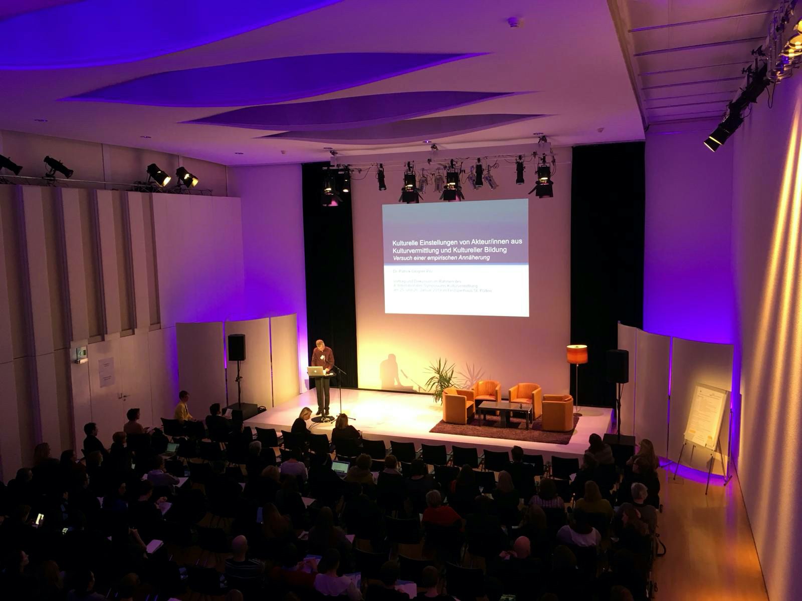 Ein Vortrag in einem Konferenzraum mit lila Beleuchtung und Publikum.