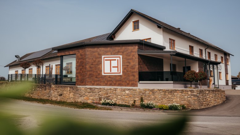 Ein modernes Gebäude mit der Aufschrift 'Gasthof Thaler', umgeben von einer Steinmauer und Pflanzen.
