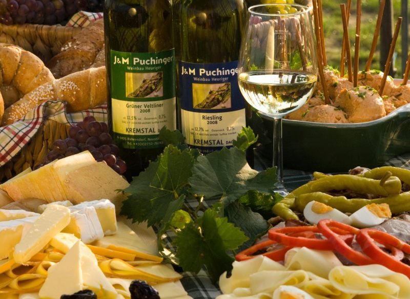 Heurigenjause mit Wein, Käse, Brot und Aufschnitt auf einem Tisch.