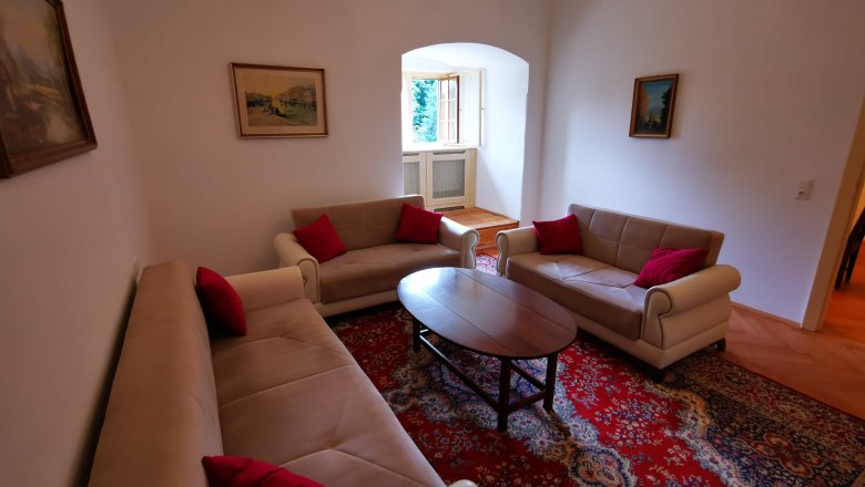 Wohnzimmer mit drei Sofas, rotem Teppich und Gemälden an den Wänden.