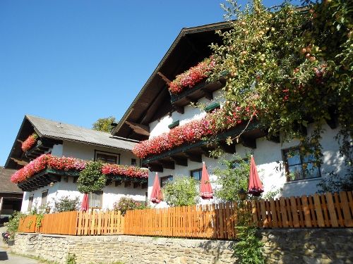 Traditionelles Bauernhaus mit Blumen an den Balkonen und einem Holzzaun im Vordergrund.