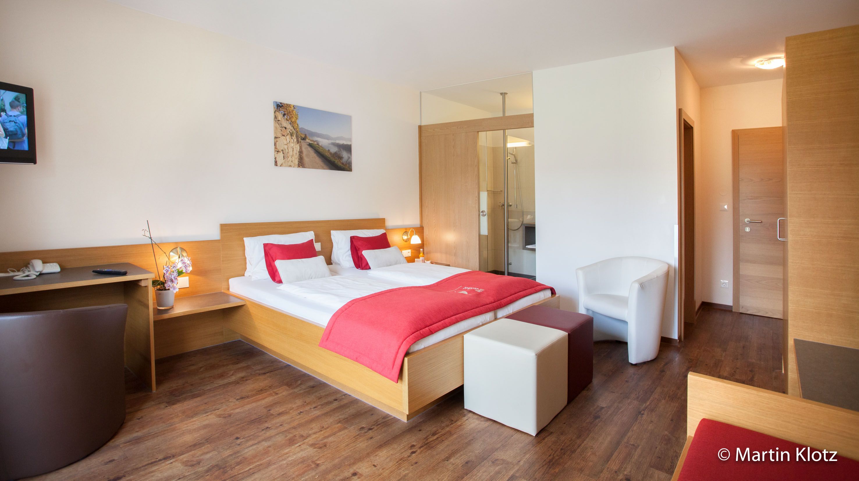 Modernes Hotelzimmer mit Doppelbett, roten Akzenten, Schreibtisch und Fernseher.