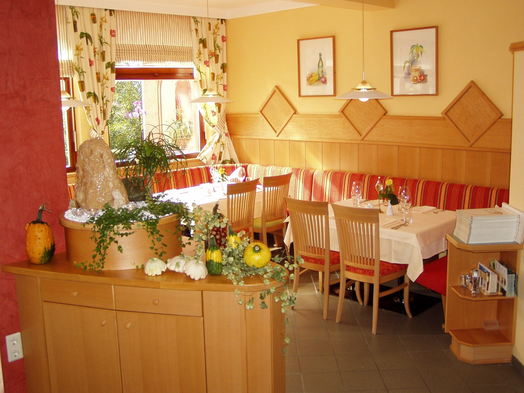 Gemütliches Restaurant mit Holzmöbeln, dekoriert mit Kürbissen und Pflanzen.