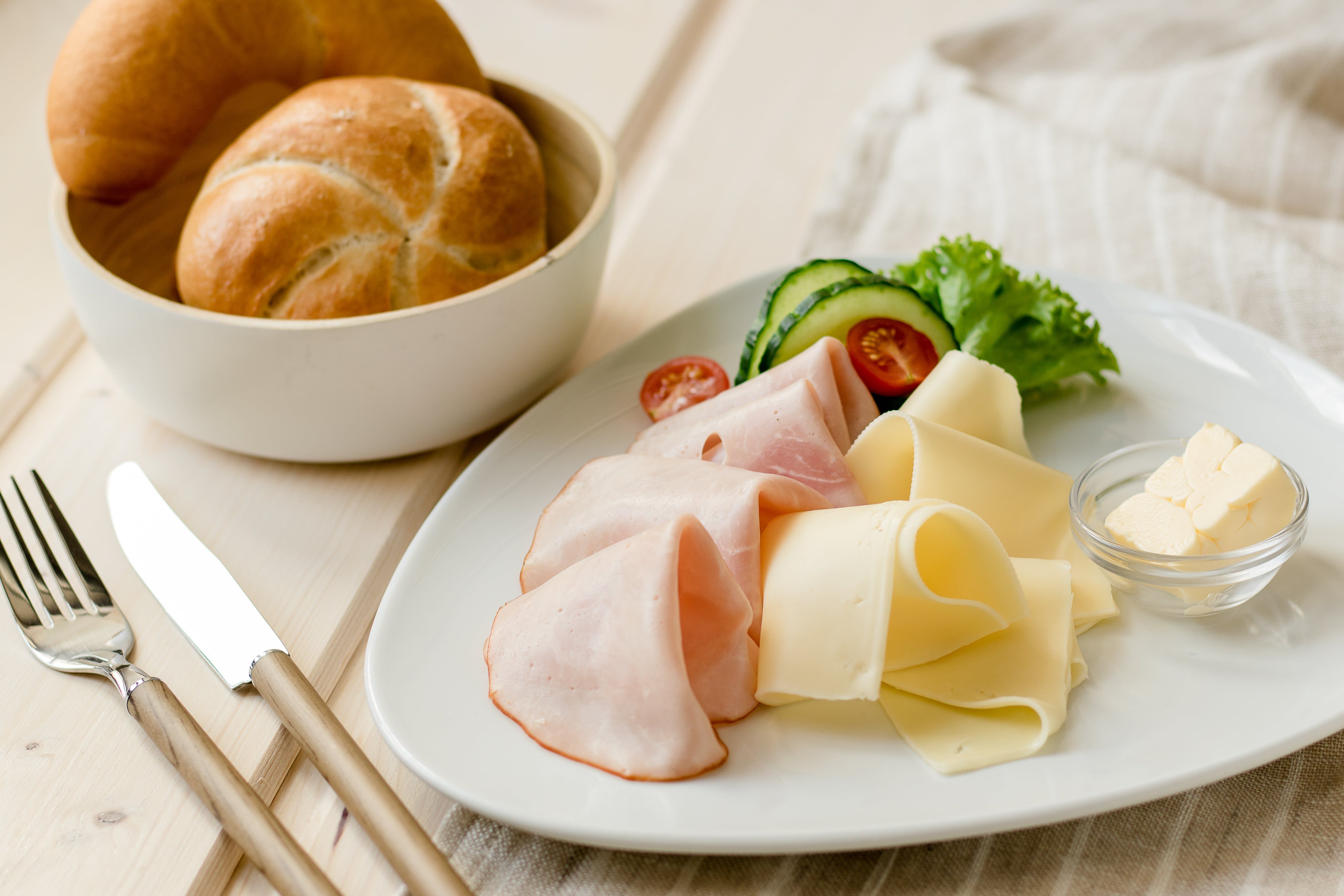Frühstücksteller mit Schinken, Käse, Gemüse und Brötchen.