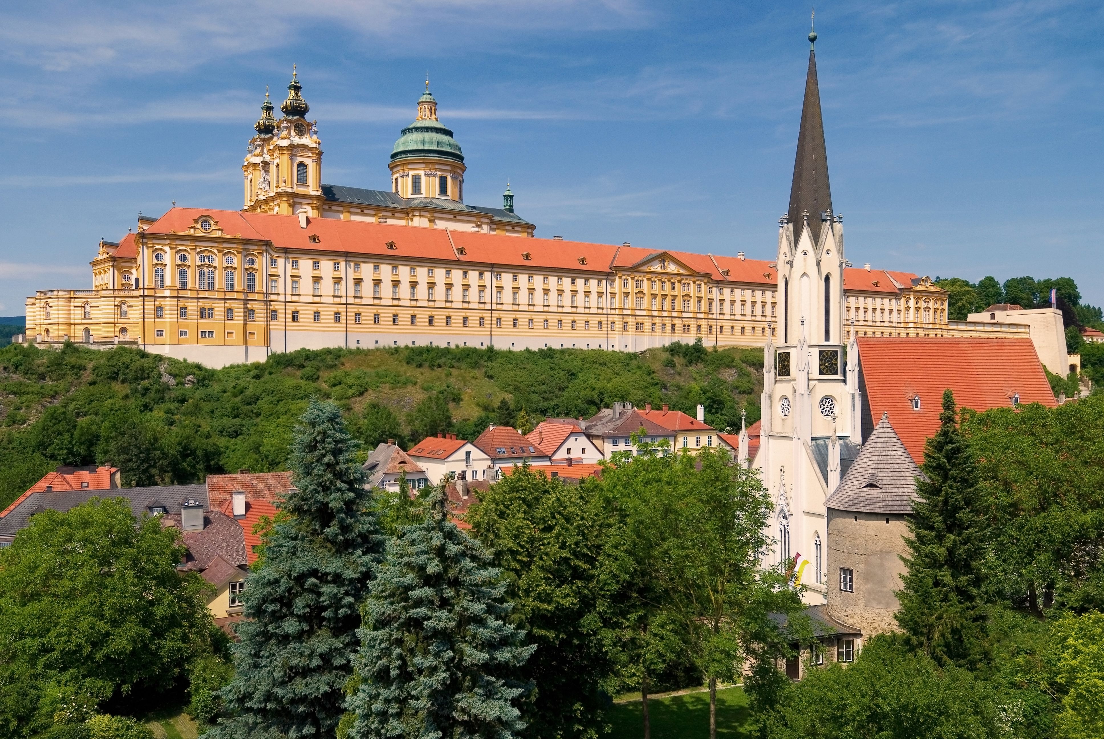 Blick auf das Stift Melk und die Pfarrkirche in Melk, umgeben von grüner Landschaft und blauen Himmel.