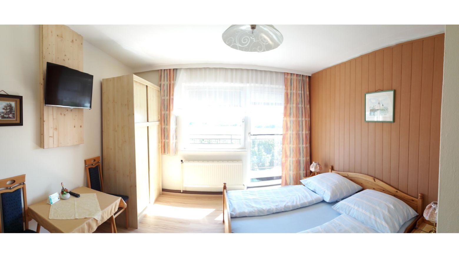 Ein gemütliches Gästezimmer mit Doppelbett, Holzmöbeln, einem kleinen Tisch und einem Fernseher an der Wand.