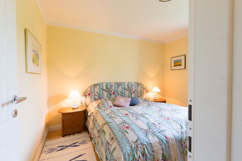 Gemütliches Schlafzimmer mit Doppelbett, blumigem Bettbezug und zwei Nachttischen mit Lampen. Gelbe Wände und Bilder an den Wänden.