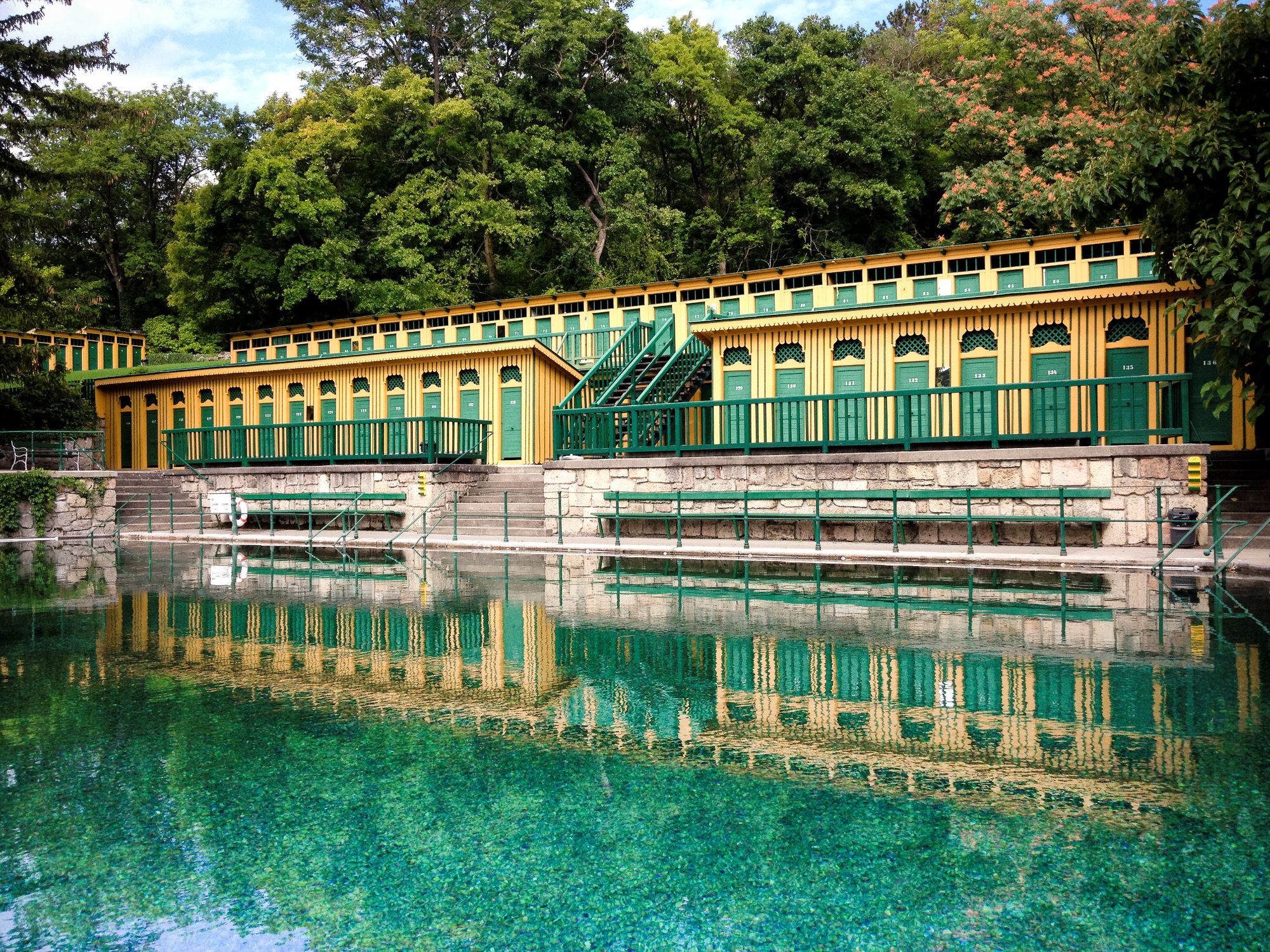 Historisches Badehaus in Bad Fischau mit grün-gelber Fassade und reflektierendem Wasser.