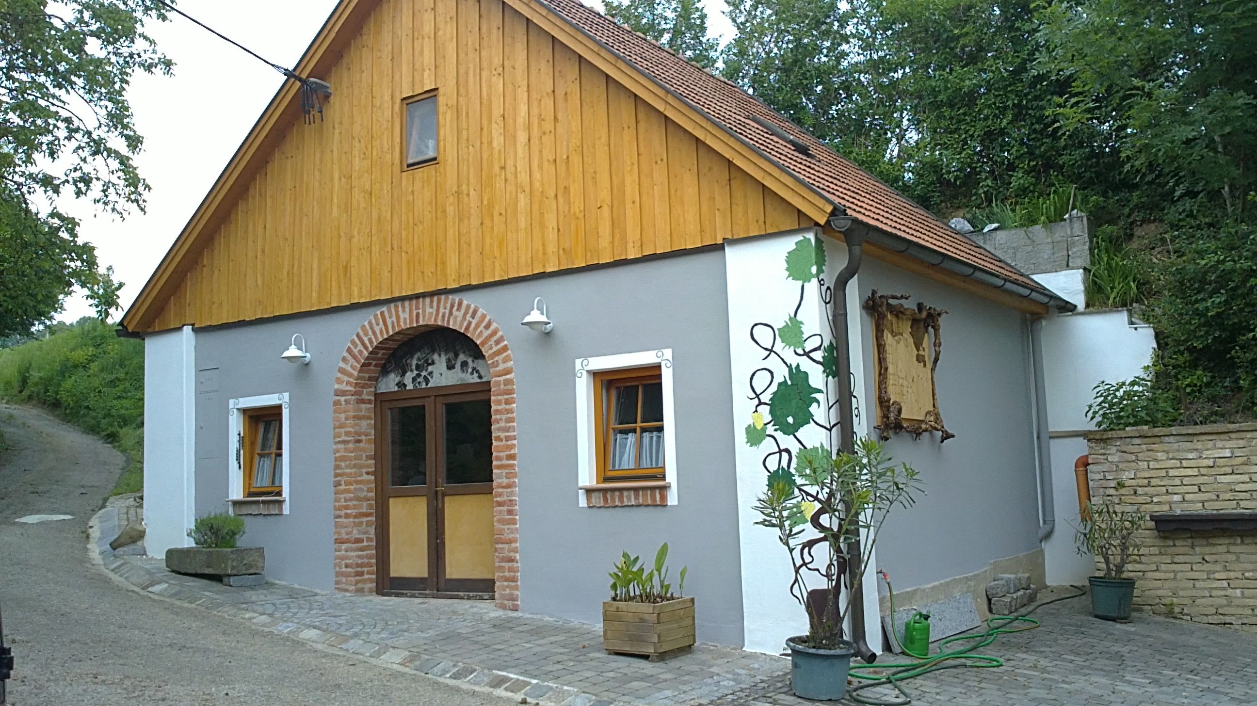 Ein traditionelles Heurigenhaus mit Holzverkleidung und Ziegelbogen, umgeben von Pflanzen.