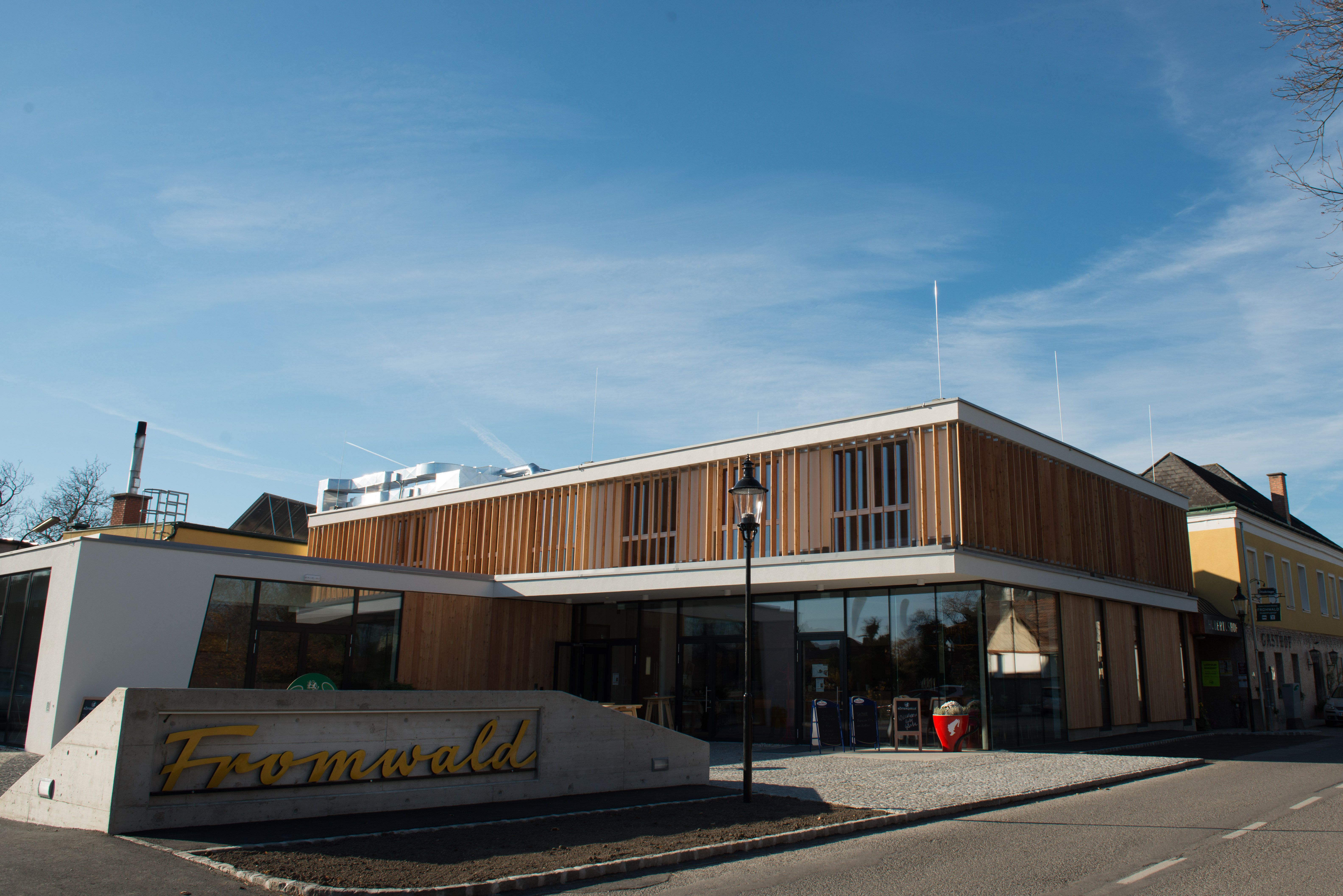 Modernes Gebäude mit Holzfassade und Glasfront, davor ein Schild mit der Aufschrift 'Fromwald'.