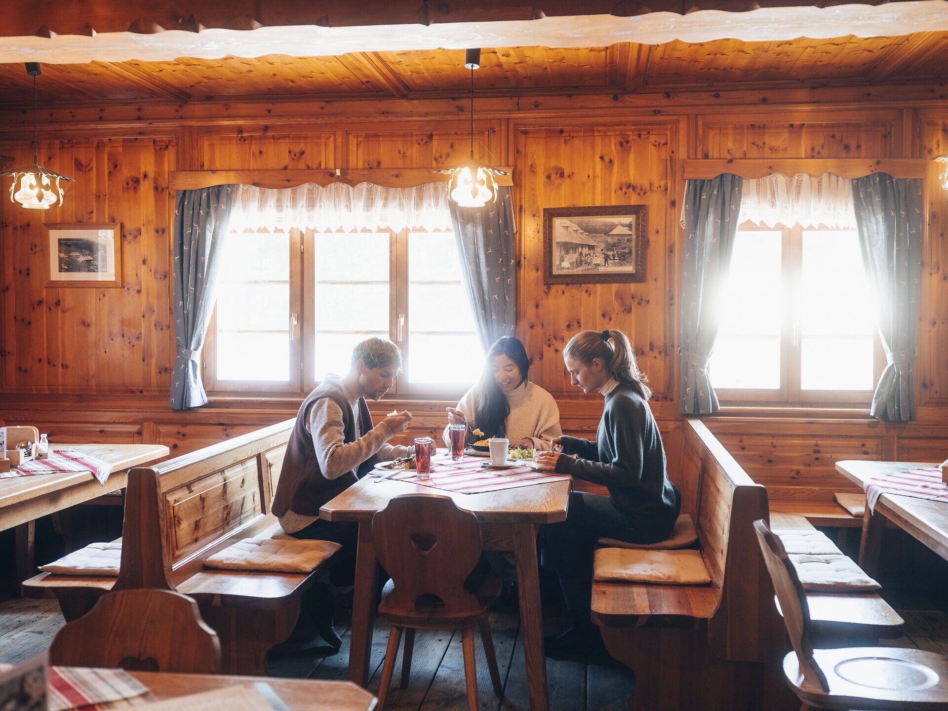 In der gemütlichen Atmosphäre einer traditionellen Hütte genießen die Gäste köstliche Speisen und die Gesellschaft von Freunden. Das warme Holzinterieur und die sanften Lichtstrahlen schaffen eine einladende Stimmung, die zum Verweilen einlädt. Hier wird der Winter in den Wiener Alpen zu einem unvergesslichen Erlebnis.