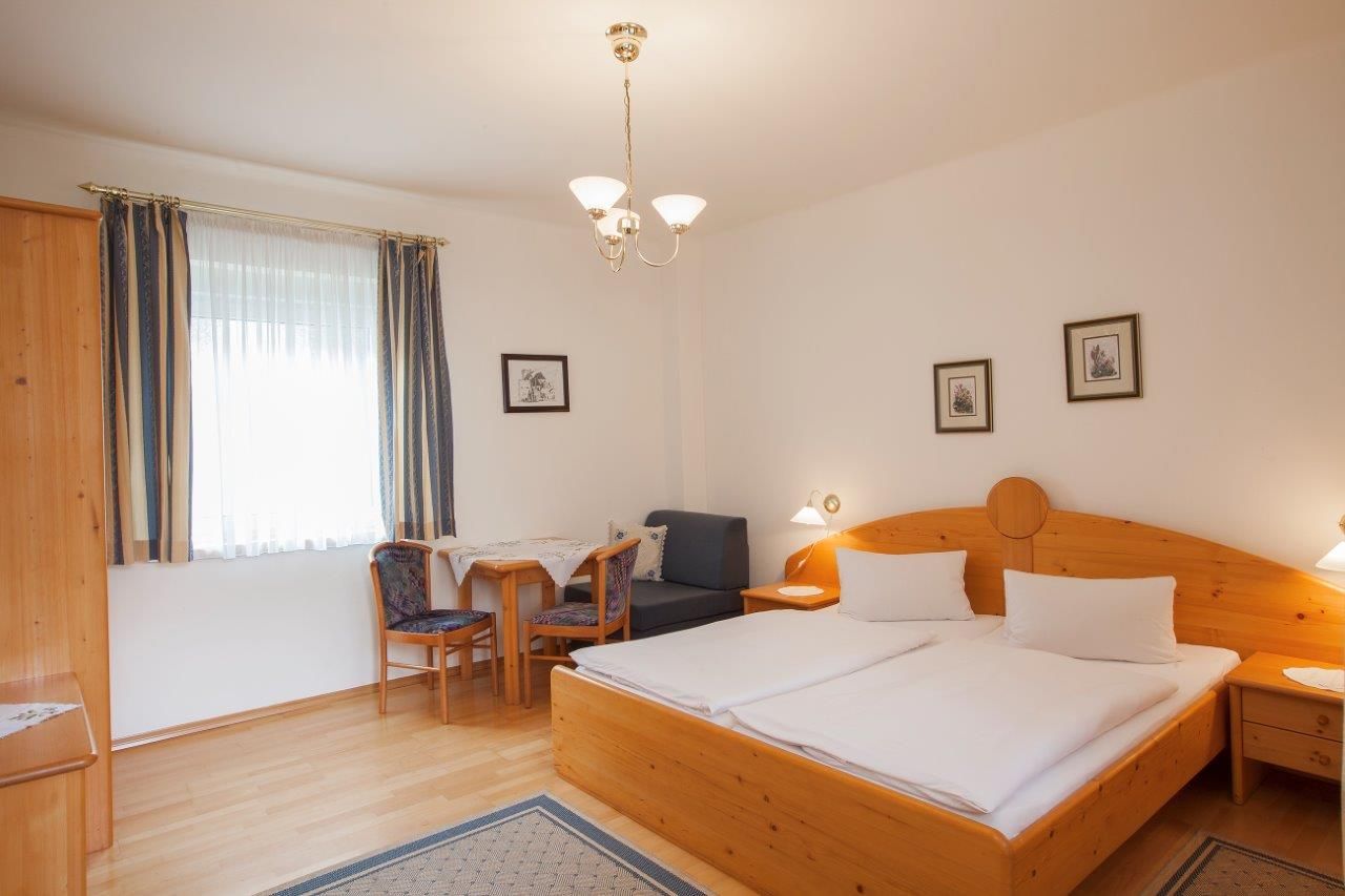 Gemütliches Zimmer mit Doppelbett, Holzmöbeln und kleinem Tisch mit Stühlen.