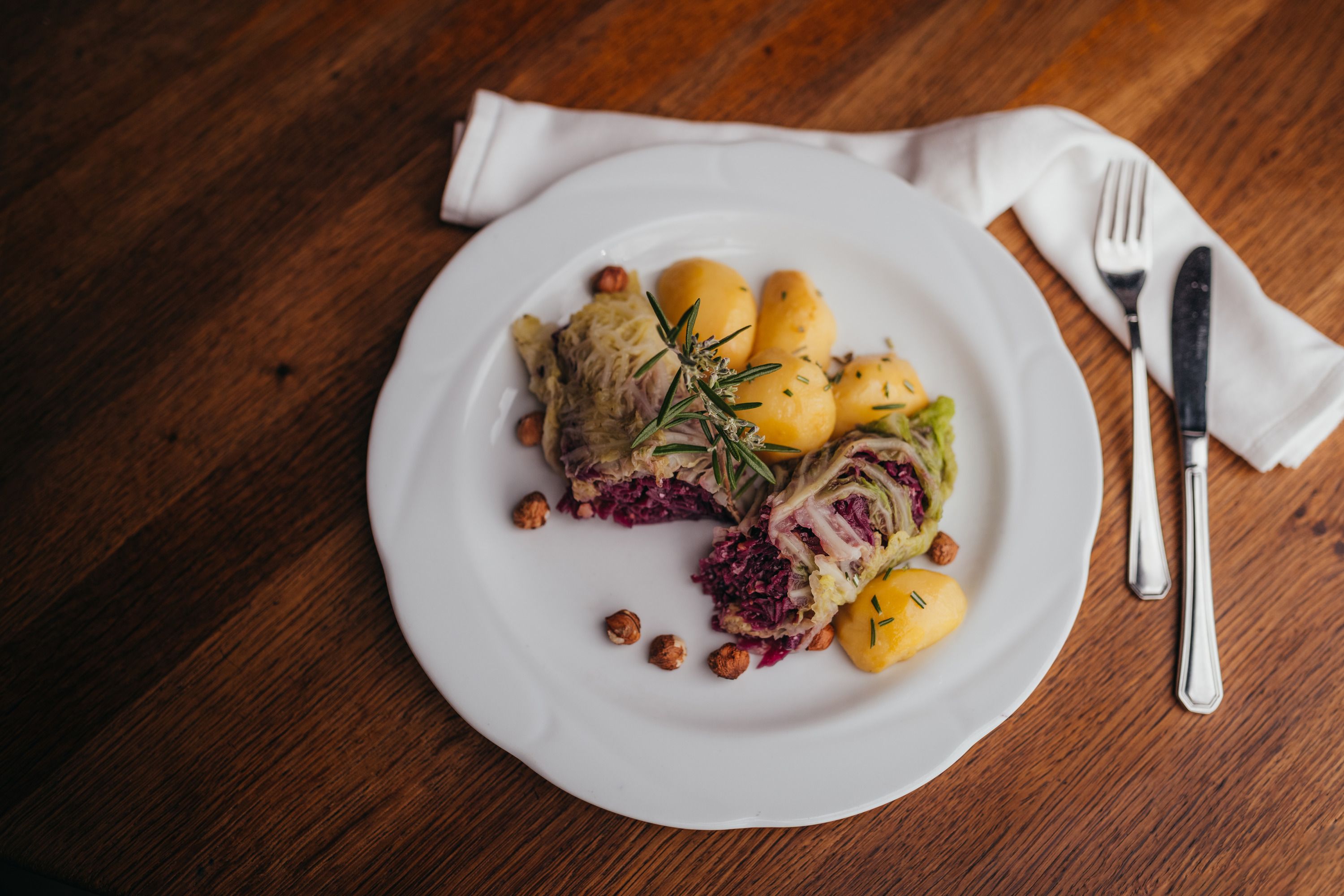 Ein Teller mit gefüllten Krautblättern, Kartoffeln und Nüssen, garniert mit Rosmarin.