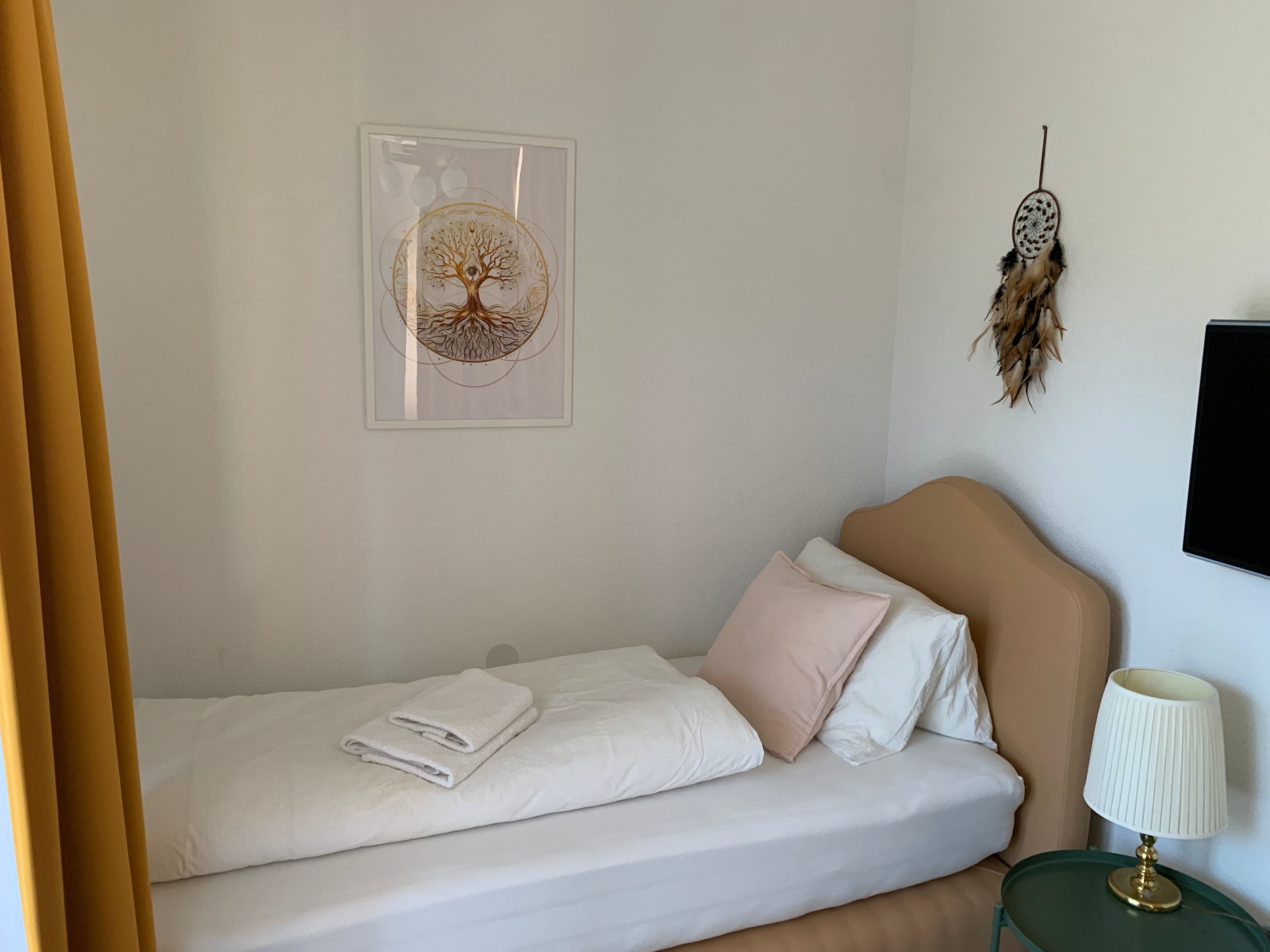 Einzelzimmer mit Bett, Traumfänger und Lampe.