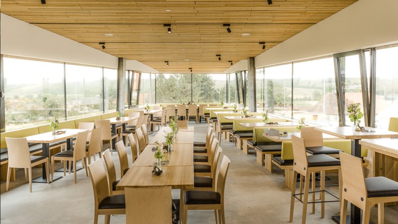 Innenansicht eines modernen Restaurants mit Holzm&ouml;beln und gro&szlig;en Fenstern.