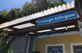 Schild mit der Aufschrift 'Eichberger Kellergasse' an einem Geb&auml;ude mit Wellblechdach.