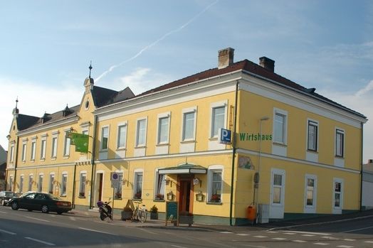 Gelbes Wirtshaus an einer Straßenecke mit mehreren Fenstern und einem Eingang.