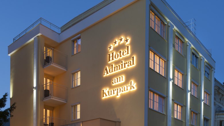 Außenansicht eines Hotels bei Dämmerung mit beleuchtetem Schriftzug "Hotel Admiral am Kurpark".