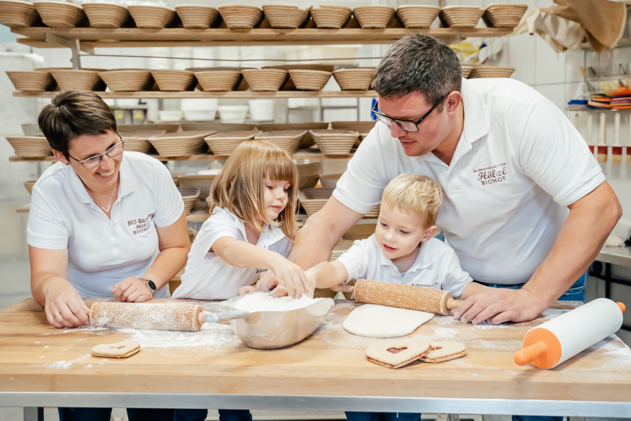 Familie beim Backen in einer Bäckerei mit vielen Brotkörben im Hintergrund.