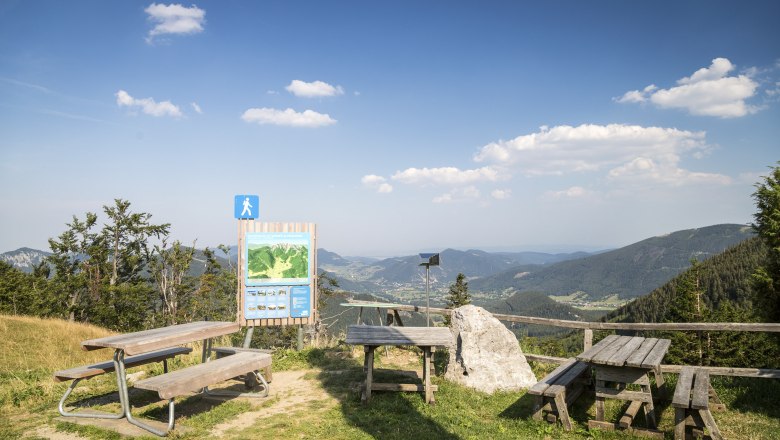Aussichtspunkt mit Holzb&auml;nken und Infotafel in den Bergen.
