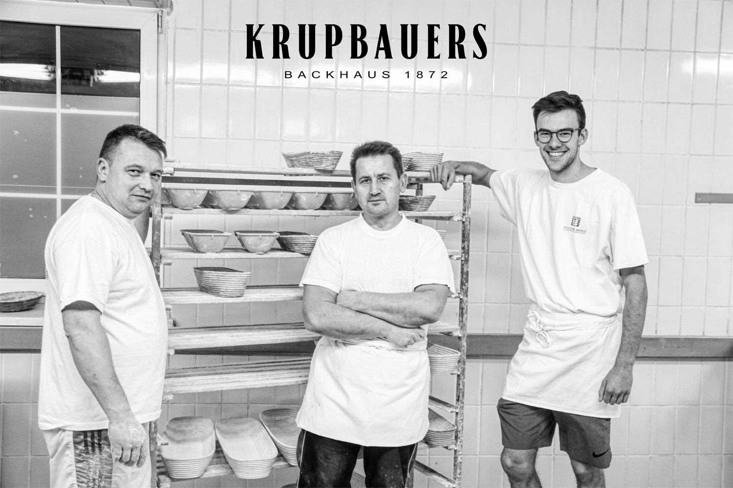 Drei Bäcker in einer Backstube mit Brotkörben im Hintergrund.