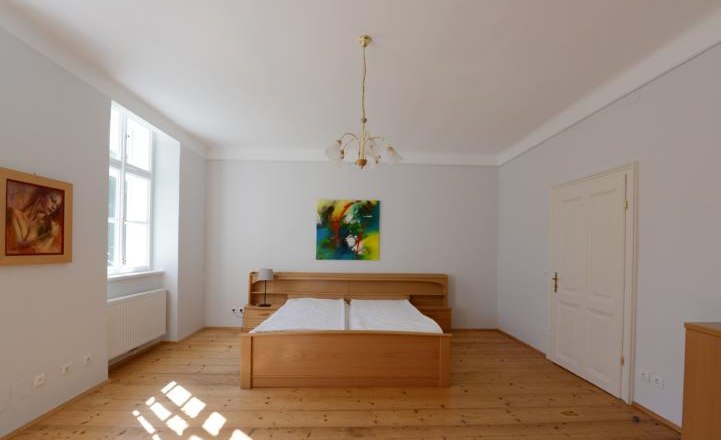Schlafzimmer mit Holzboden, Doppelbett, zwei Gemälden und einem Fenster.