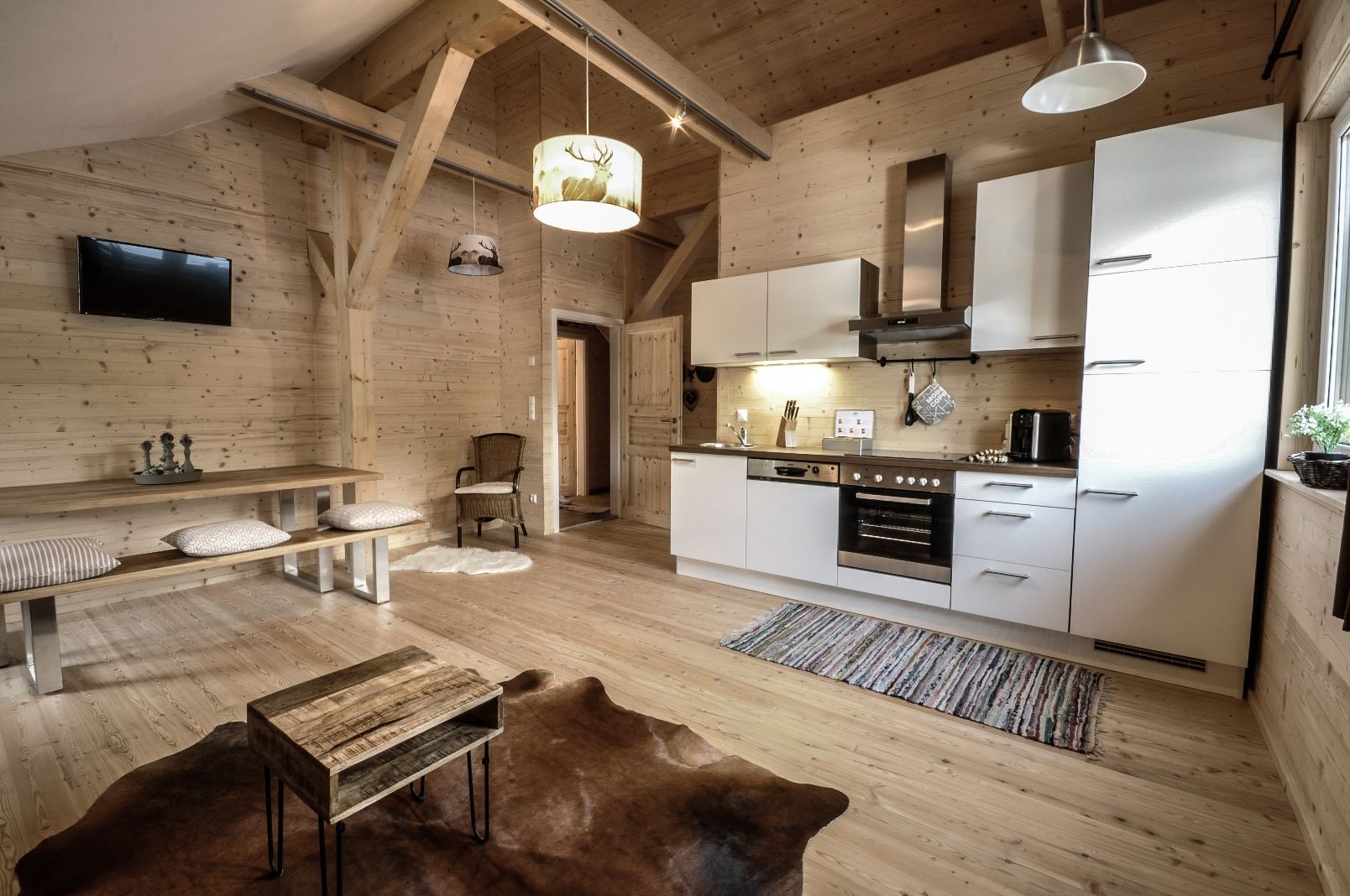 Gemütliches Apartment mit Holzwänden, moderner Küche, Esstisch und Fernseher. Rustikaler Stil mit Teppich und Holzmöbeln.