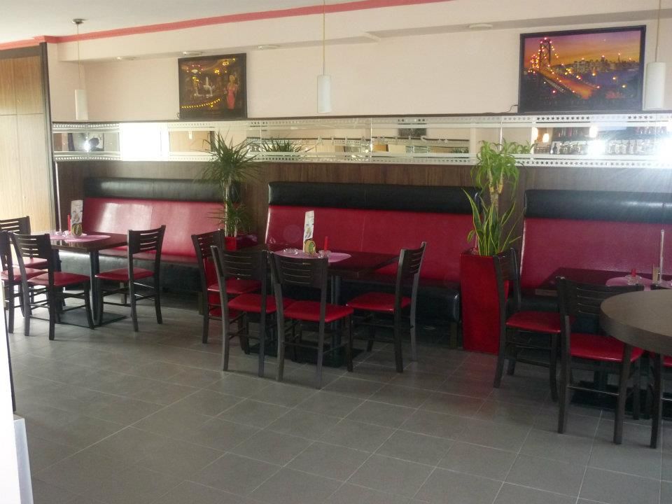 Innenansicht eines Cafés mit roten Sitzbänken und schwarzen Stühlen.