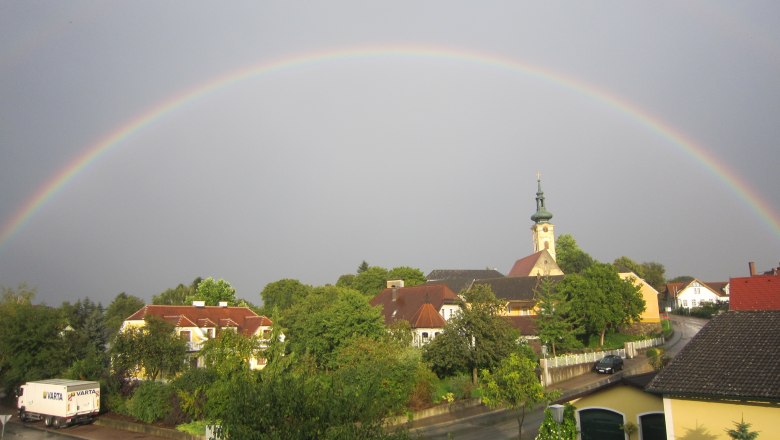 Ein Regenbogen spannt sich &uuml;ber ein Dorf mit Kirche und H&auml;usern in Gerersdorf.