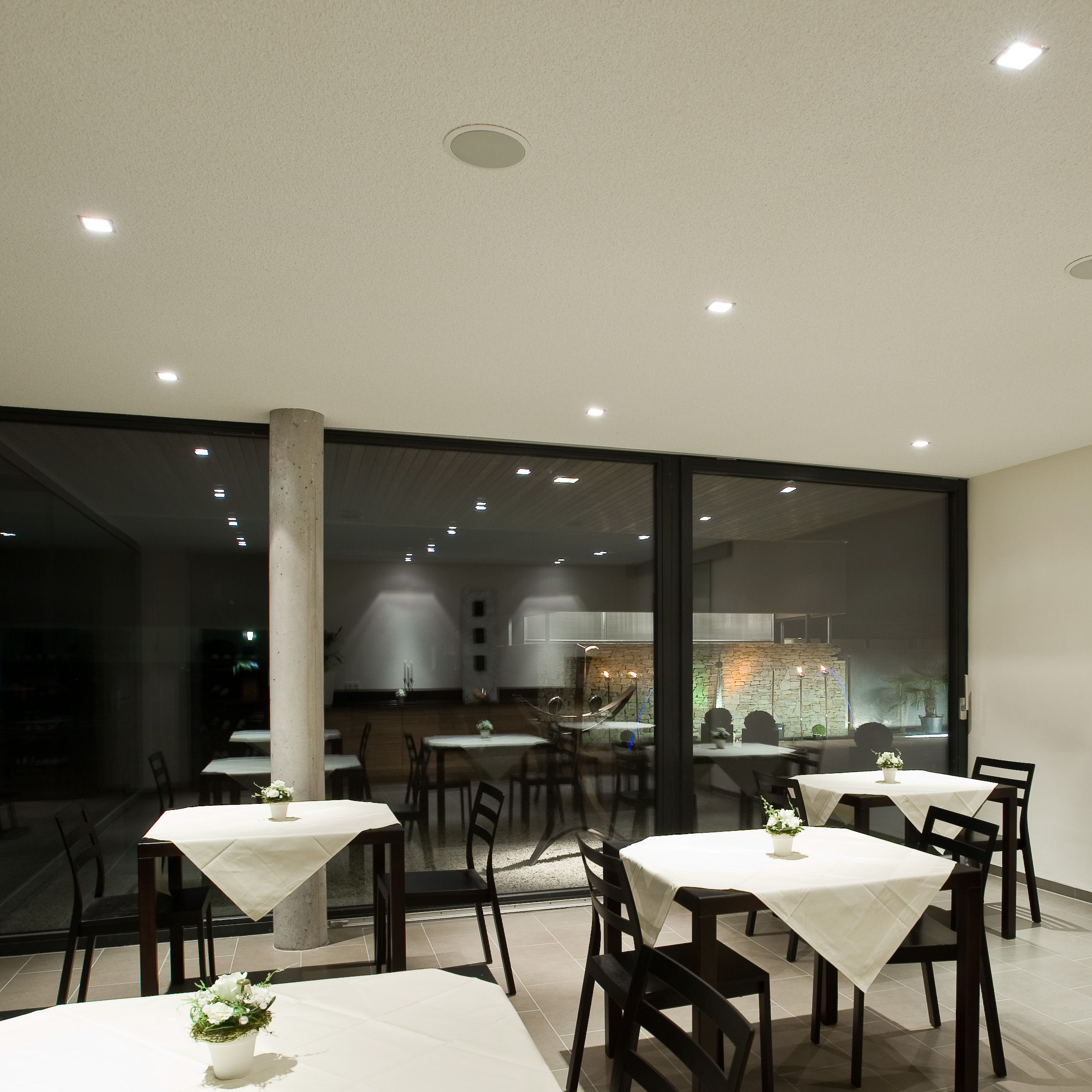 Moderner Frühstücksraum mit Tischen und Stühlen, dekoriert mit weißen Tischdecken und Blumen.