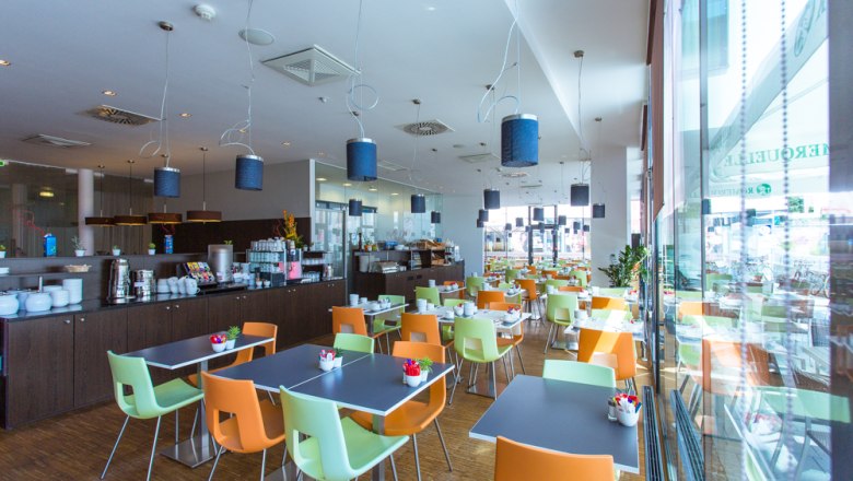 Moderner Fr&uuml;hst&uuml;cksraum mit bunten St&uuml;hlen und gedeckten Tischen.