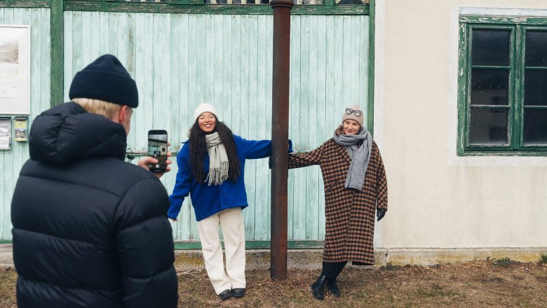 Zwei fr&ouml;hliche Frauen posieren vor der charmanten Kulisse des Bahnhofs der H&ouml;llental Museumseisenbahn. Umgeben von der winterlichen Landschaft der Wiener Alpen strahlen sie Lebensfreude und Abenteuerlust aus. Die rustikale Architektur und die sanfte Schneedecke schaffen eine einladende Atmosph&auml;re f&uuml;r alle, die die Sch&ouml;nheit der Natur erleben m&ouml;chten.