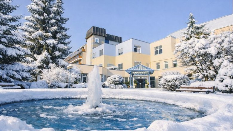 Ein Gesundheitsresort im Winter mit schneebedeckten B&auml;umen und einem gefrorenen Brunnen im Vordergrund.