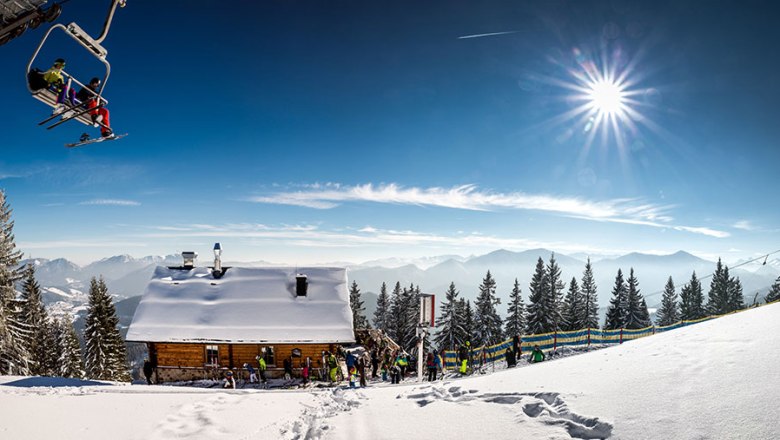 Winterlandschaft mit Skih&uuml;tte, Sessellift und Bergen im Hintergrund.
