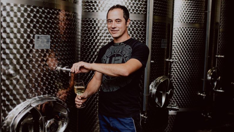 Mann zapft Wein aus einem Edelstahltank in einem Weinkeller.